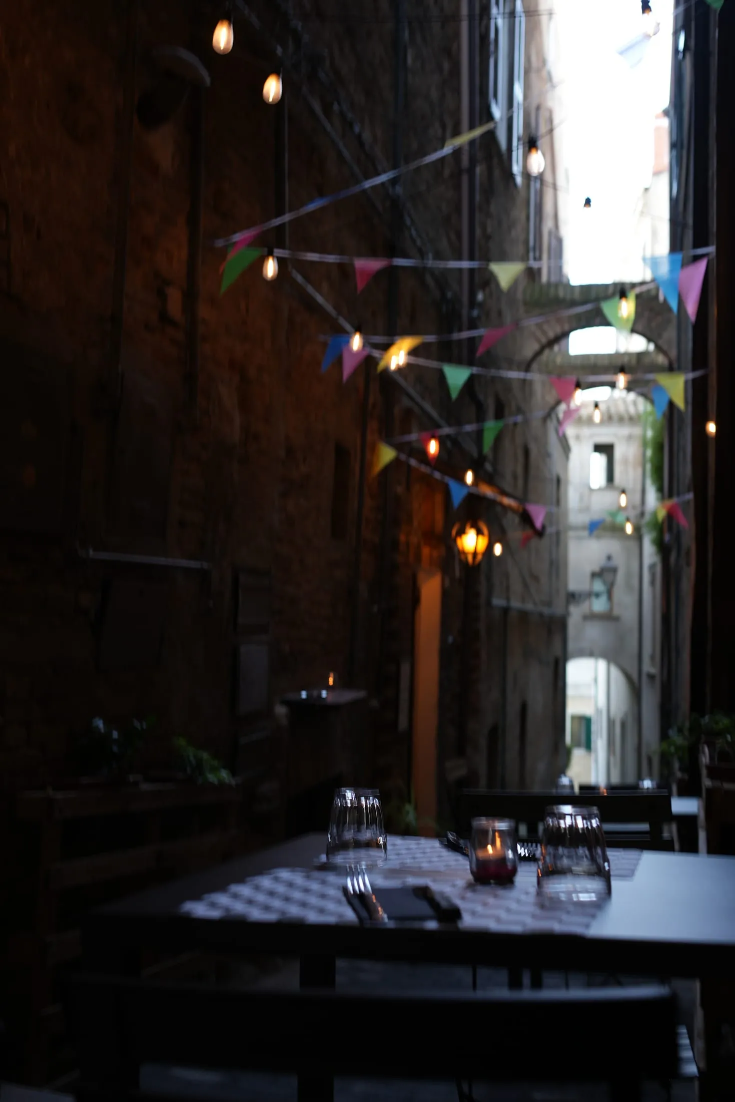 Tavolo apparecchiato a lume di candela nel vicolo, sotto le bandierine e le luci del borgo